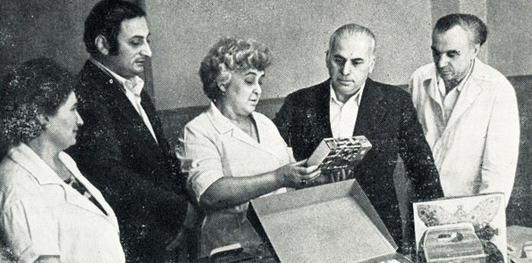 Старший инженер-титестер В. Р. Схиртладзе (третья слева) и начальник грузинского промышленного объединения 'Чай-Грузия' Э. С. Малазония (второй справа) рассматривают новые образцы упаковки грузинского чая